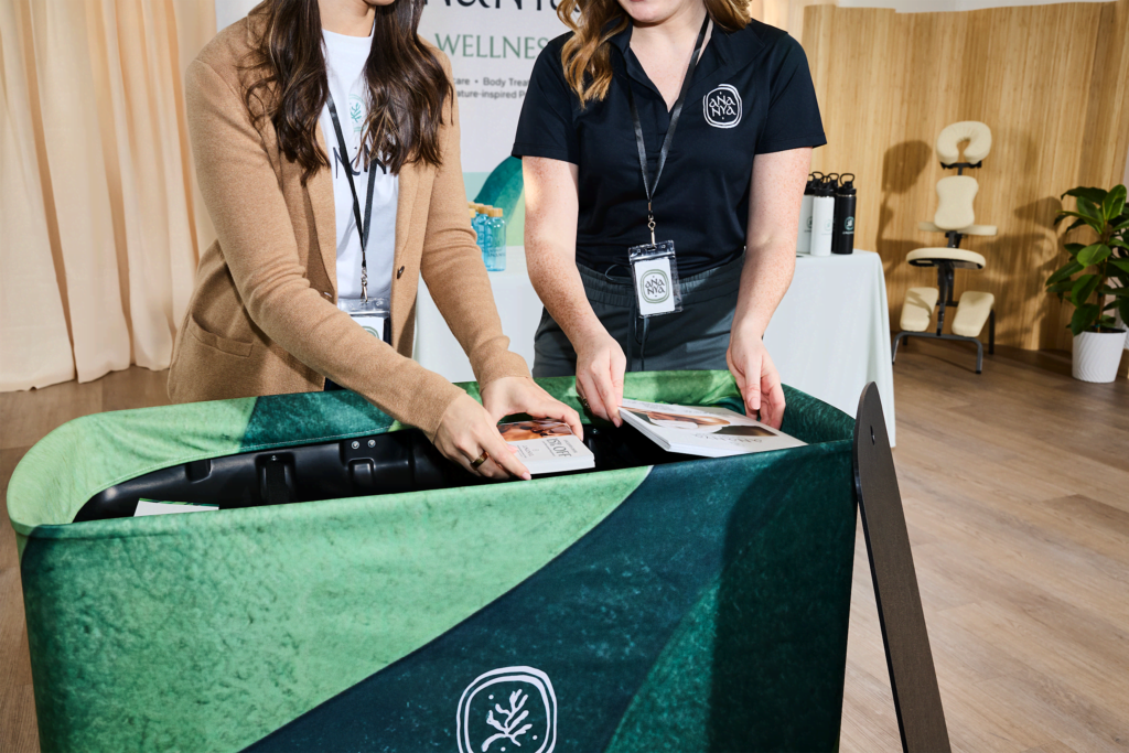 Two small business owners at Ananya wellness stand reviewing leaflets at a trade show table with a green velvet tablecloth.