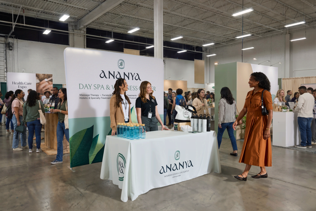 Ananya Day Spa & Wellness Centre trade show stand, featuring a staff member and visitors at a healthcare expo.